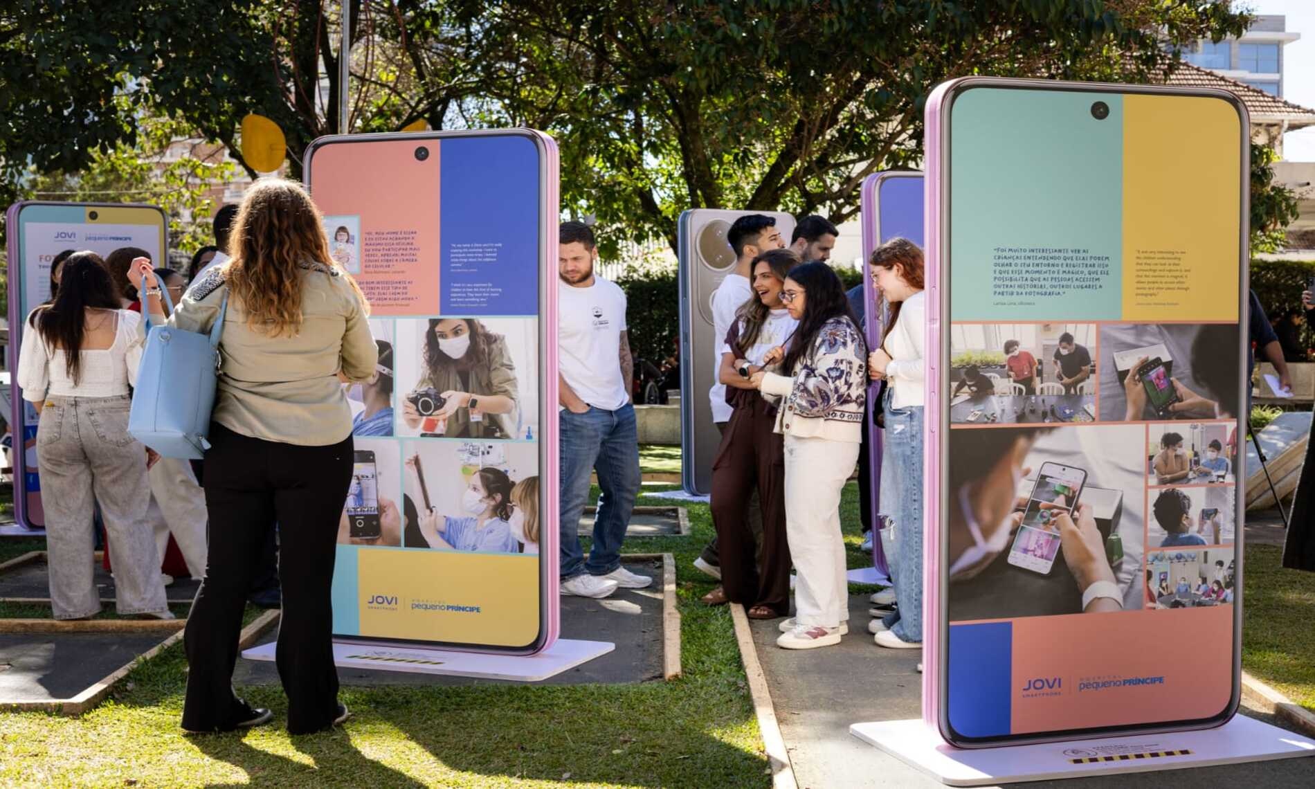 Visitantes participam de exposição promovida pela JOVI em parceria com o Hospital Pequeno Príncipe, com instalações em formato de smartphones exibindo histórias, fotografias e conteúdos interativos.